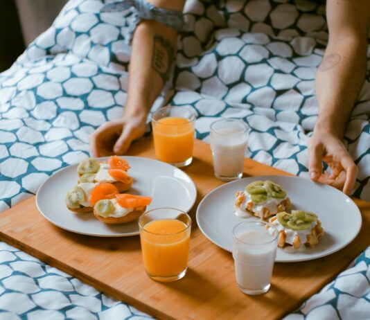 여행 중 건강 유지: 쉽고 간편한 팁 person serving pastries on white ceramic plates with fruit juice glasses on wooden tray on top of bed