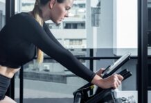 실내에서 즐기는 유산소 운동의 장점 a woman on a stationary bike using a tablet