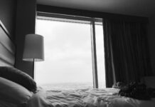 grayscale photo of bed near white table lamp