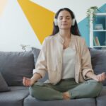 집에서 즐기는 ‘마음 챙김 스트레칭’, 일상에 활력을 더하다 Woman meditating on couch with headphones on