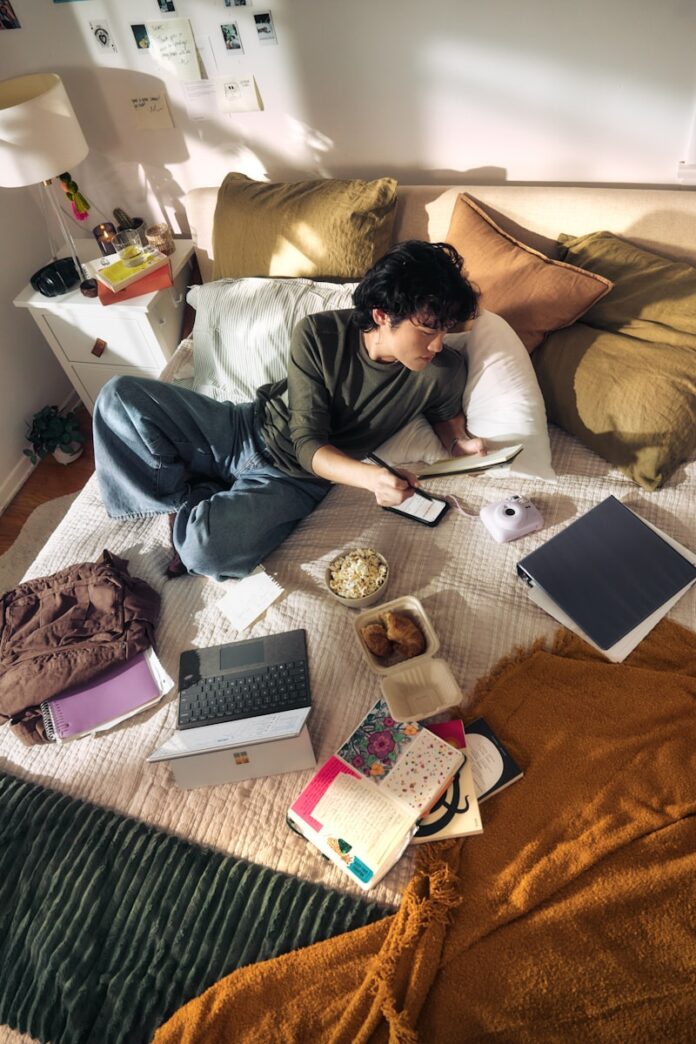 Young man on bed with laptop and snacks