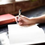 “스트레스, 자연스럽게 풀기… 새롭게 떠오르는 ‘슬로우 라이프’ 실천 팁” a person writing on a piece of paper with a pen