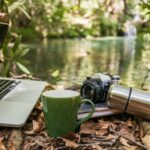“잘 자야 내일이 가볍다”…당신의 수면 습관, 최신 트렌드로 바꿔볼 때 Laptop, camera, and mug by a forest stream